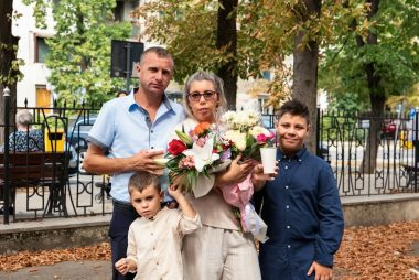 A family of four standing together in a park with a large flower bouquet